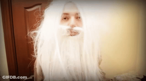 A Woman With Long White Hair And A Beard Looks At The Camera GIF