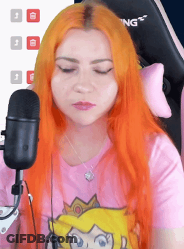 A Woman With Orange Hair Is Sitting In Front Of A Microphone Wearing A Pink Shirt That Says Princess Peach GIF