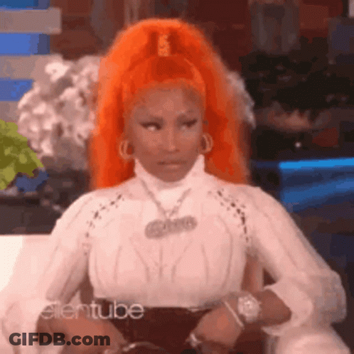 A Woman With Orange Hair Is Sitting On A Couch Wearing A White Shirt . GIF