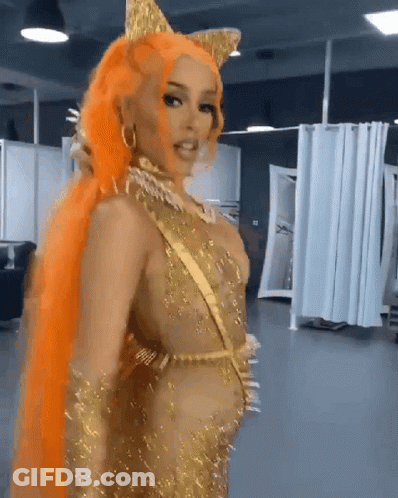 A Woman With Orange Hair Is Wearing A Gold Costume GIF