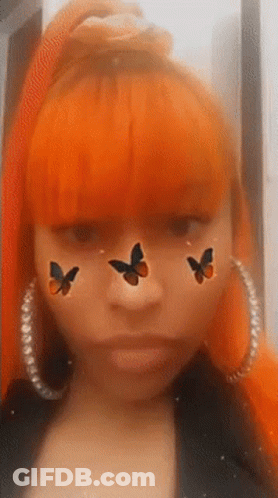 A Woman With Orange Hair Is Wearing Hoop Earrings And Has Three Butterflies On Her Face . GIF