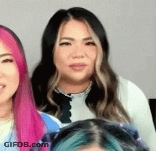 A Woman With Pink And Blue Hair Is Standing Next To Another Woman . GIF