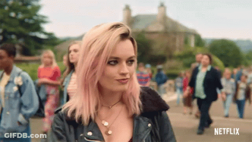 A Woman With Pink Hair And A Leather Jacket Is Standing In Front Of A Crowd . GIF