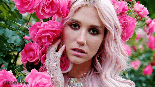A Woman With Pink Hair And Gloves Is Surrounded By Pink Roses In A Garden . GIF