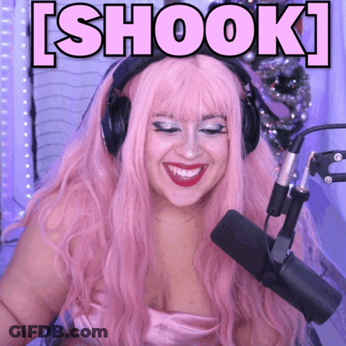 A Woman With Pink Hair And Headphones Is Smiling In Front Of A Microphone With The Words Shook Above Her GIF