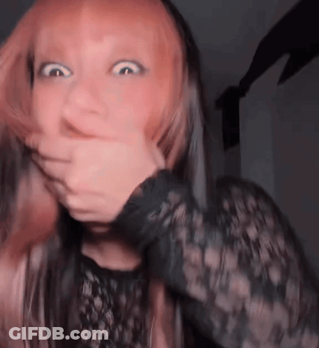 A Woman With Pink Hair Is Covering Her Mouth With Her Hand . GIF