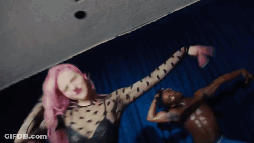 A Woman With Pink Hair Is Dancing Next To A Man With No Shirt On GIF