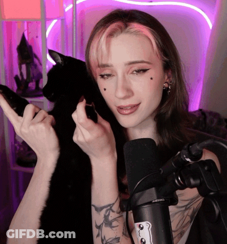 A Woman With Pink Hair Is Holding A Black Cat In Front Of A Microphone That Says Seiko GIF