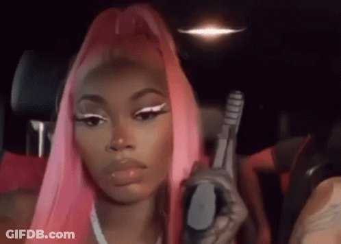 A Woman With Pink Hair Is Holding A Gun While Sitting In A Car . GIF