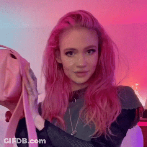 A Woman With Pink Hair Is Holding A Pink Purse In Her Hands . GIF