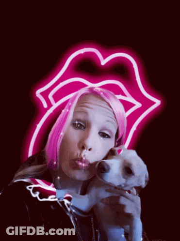 A Woman With Pink Hair Is Holding A Small Dog In Front Of A Neon Sign That Says Rolling Stones GIF