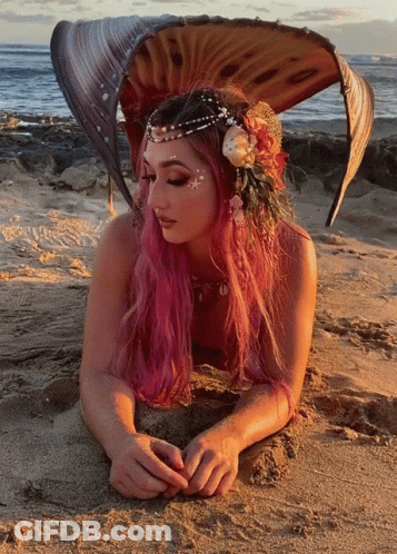A Woman With Pink Hair Is Laying On A Sandy Beach GIF