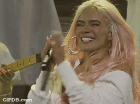 A Woman With Pink Hair Is Singing Into A Microphone And Smiling GIF