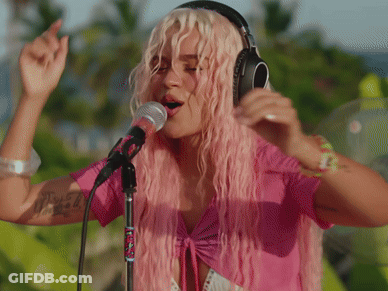 A Woman With Pink Hair Is Singing Into A Microphone And Wearing Headphones GIF