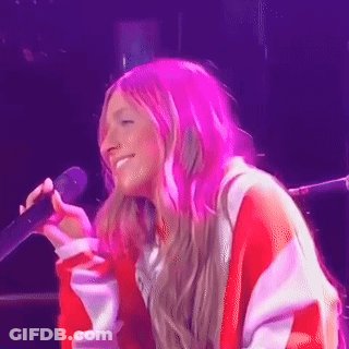 A Woman With Pink Hair Is Singing Into A Microphone On A Stage GIF