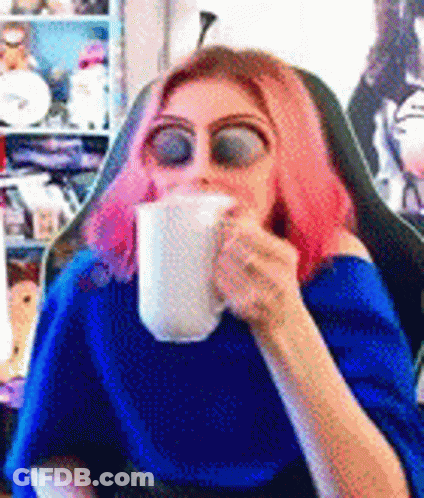 A Woman With Pink Hair Is Sitting In A Chair Drinking From A Mug . GIF