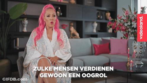 A Woman With Pink Hair Is Sitting In Front Of A Couch And A Videoland Logo GIF