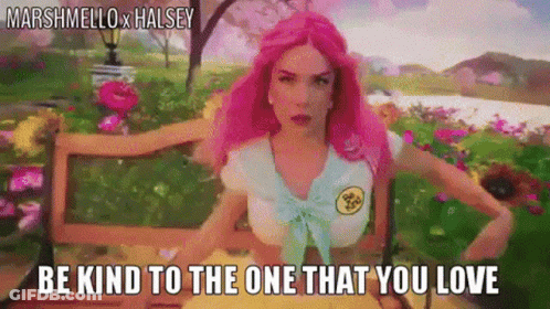 A Woman With Pink Hair Is Sitting On A Bench With Flowers In The Background . GIF