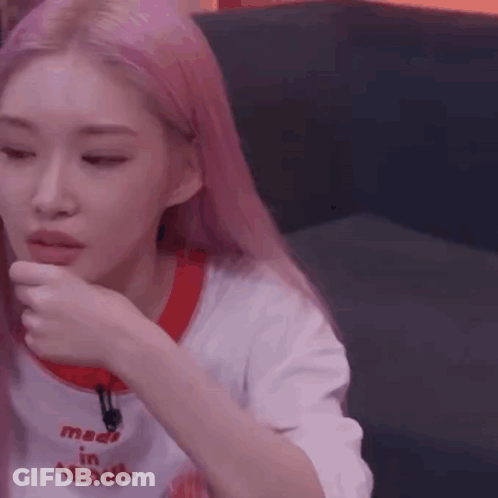 A Woman With Pink Hair Is Sitting On A Couch With Her Hand To Her Face . GIF