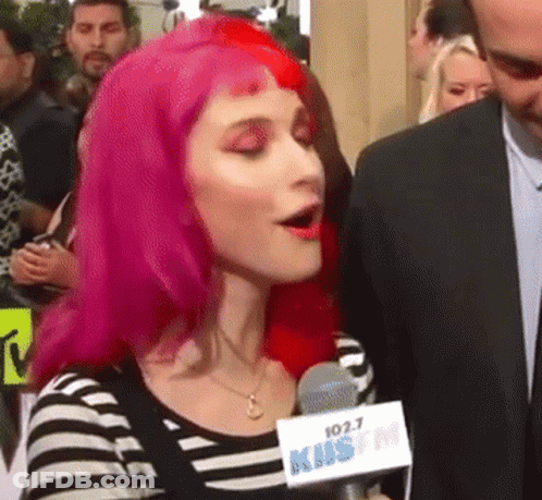 A Woman With Pink Hair Is Speaking Into A Microphone That Says 102.7 Kms Fm GIF