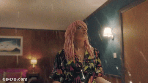 A Woman With Pink Hair Is Standing In A Room In The Rain GIF
