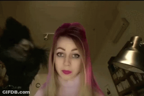A Woman With Pink Hair Is Standing In Front Of A Lamp And A Black Cat . GIF