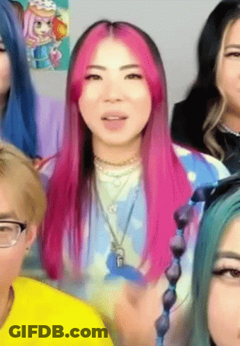 A Woman With Pink Hair Is Surrounded By Other People . GIF