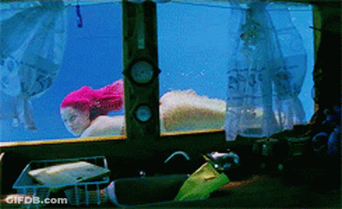 A Woman With Pink Hair Is Swimming Underwater In A Tank GIF