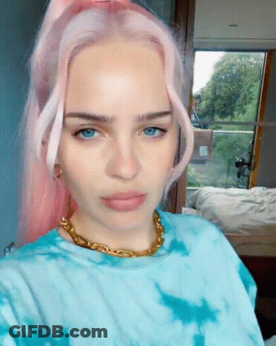 A Woman With Pink Hair Is Wearing A Blue Tie Dye Shirt And A Gold Chain Around Her Neck GIF