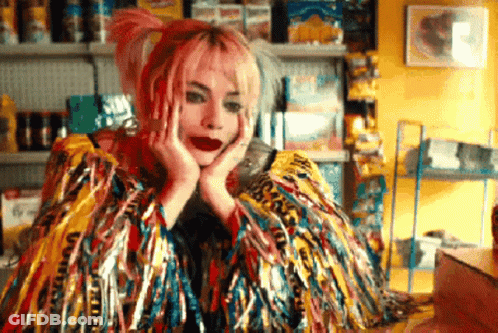 A Woman With Pink Hair Is Wearing A Colorful Feathered Coat GIF