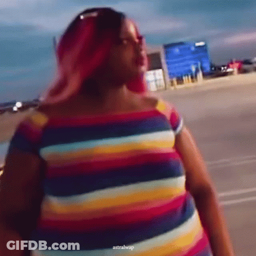 A Woman With Pink Hair Is Wearing A Colorful Striped Dress GIF