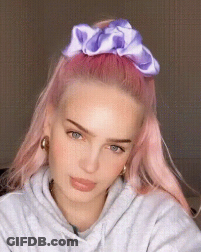 A Woman With Pink Hair Is Wearing A Purple Scrunchie In Her Hair GIF