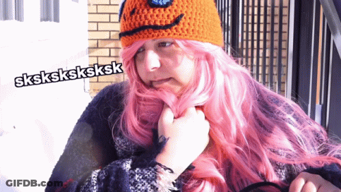 A Woman With Pink Hair Is Wearing An Orange Crocheted Hat GIF