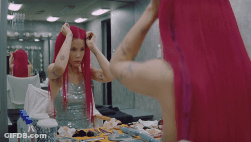 A Woman With Pink Hair Looks At Herself In The Mirror GIF