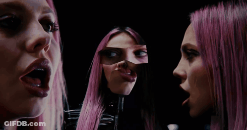 A Woman With Pink Hair Looks At Herself In The Mirror GIF