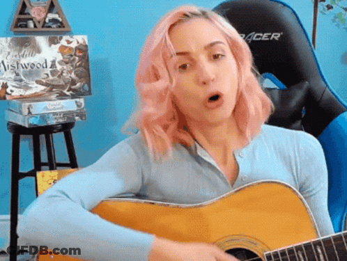 A Woman With Pink Hair Playing A Guitar In Front Of A Acer Chair GIF