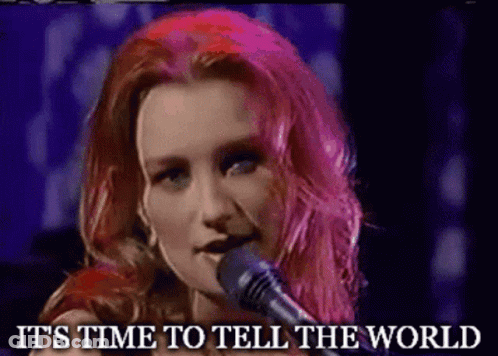 A Woman With Pink Hair Singing Into A Microphone With The Words " It 'S Time To Tell The World " Written Below Her GIF
