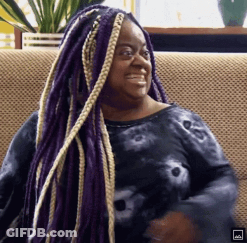 A Woman With Purple Braids Is Smiling And Sitting On A Couch GIF