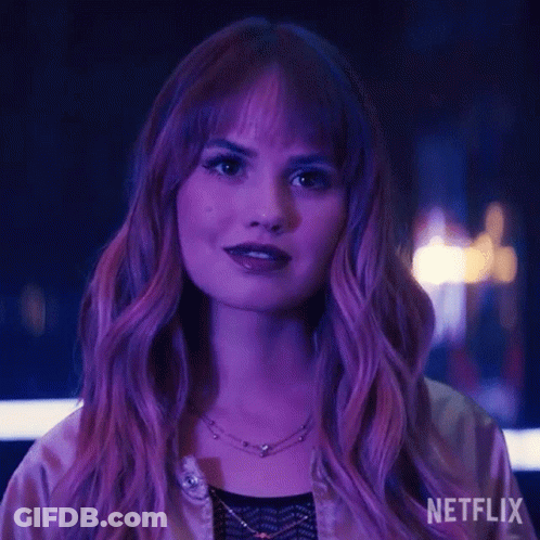 A Woman With Purple Hair And A Necklace Is Standing In Front Of A Purple Light . GIF