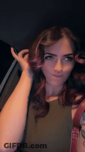 A Woman With Purple Hair And A Tattoo On Her Arm Looks At The Camera GIF