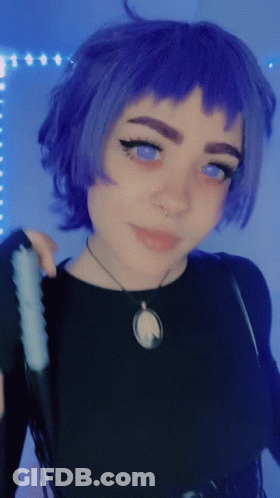 A Woman With Purple Hair And Blue Eyes Is Wearing A Black Top And A Necklace GIF
