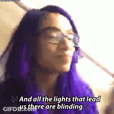 A Woman With Purple Hair And Glasses Is Singing A Song . GIF