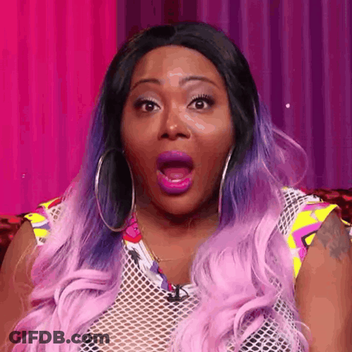 A Woman With Purple Hair And Hoop Earrings Is Making A Surprised Face With Her Mouth Open . GIF