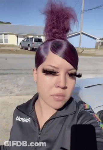 A Woman With Purple Hair And Long Eyelashes Is Standing In Front Of A Car In A Parking Lot . GIF