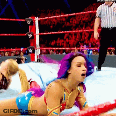 A Woman With Purple Hair Is Laying On The Ground In A Wrestling Ring GIF