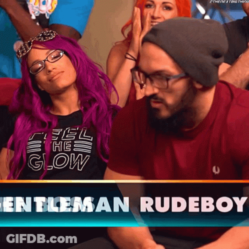 A Woman With Purple Hair Is Sitting Next To A Man Wearing Glasses And A Beanie GIF
