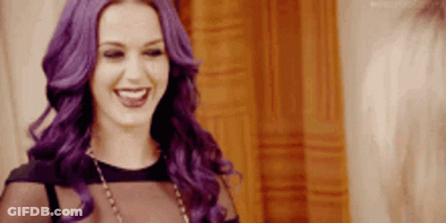 A Woman With Purple Hair Is Smiling And Wearing A Black Top And Necklace . GIF