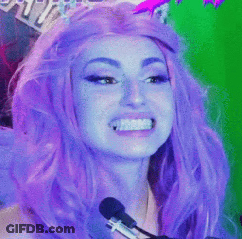 A Woman With Purple Hair Is Smiling In Front Of A Microphone While Wearing A Purple Wig . GIF