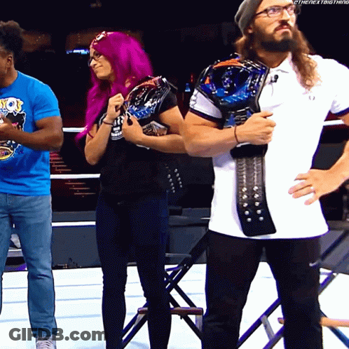 A Woman With Purple Hair Is Standing Next To A Man With A Beard Holding A Championship Belt GIF
