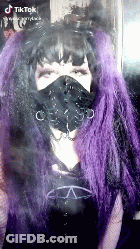 A Woman With Purple Hair Is Wearing A Black Face Mask GIF